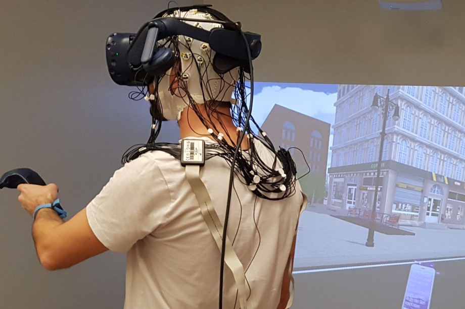 The world a test participant is experiencing wearing the HMD VR over an EEG cap is projected onto a large, screen-based CAVE VR system (© GIVA)